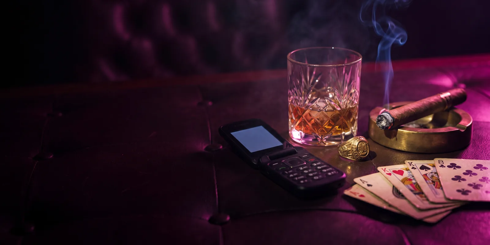 The Syndicate: a dimly lit table with whisky, a burner phone, a cigar and playing cards